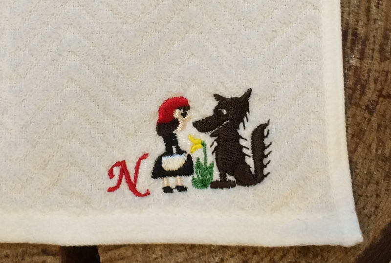 赤ずきんちゃんとオオカミの刺繍図案と筆記体のNを刺繍したハンカチ